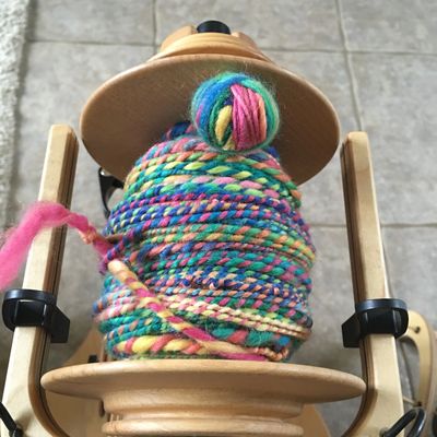 A colorful ball of yarn on a wooden spinning wheel.