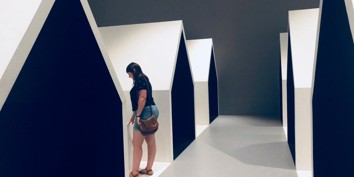Woman exploring modern, minimalistic house-shaped structures in a gallery.