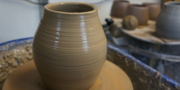 a freshly thrown curvy pot sitting glistening on the wheel, with more thrown pots in background
