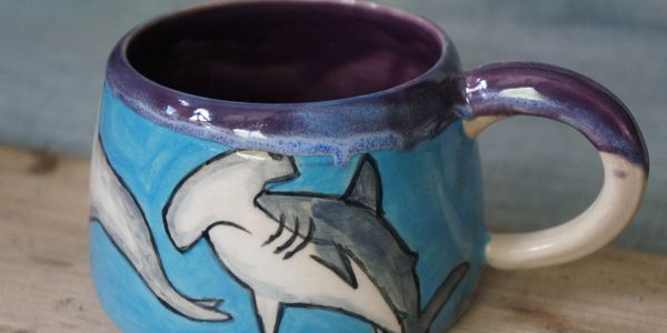 A hand painted hammerhead shark mug with blue background and purple rim