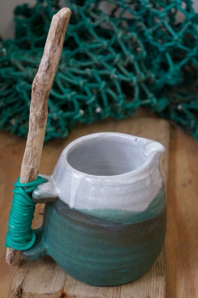 a curvy green jug with white rim , driftwood handle held on with green ghost rope