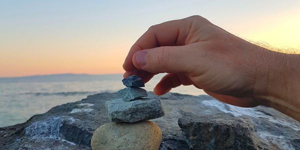 A hand carefully building a stone structure with a background of ocean view @ sunset