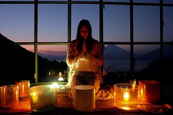 A person meditates surrounded by glowing crystal singing bowls at dusk.