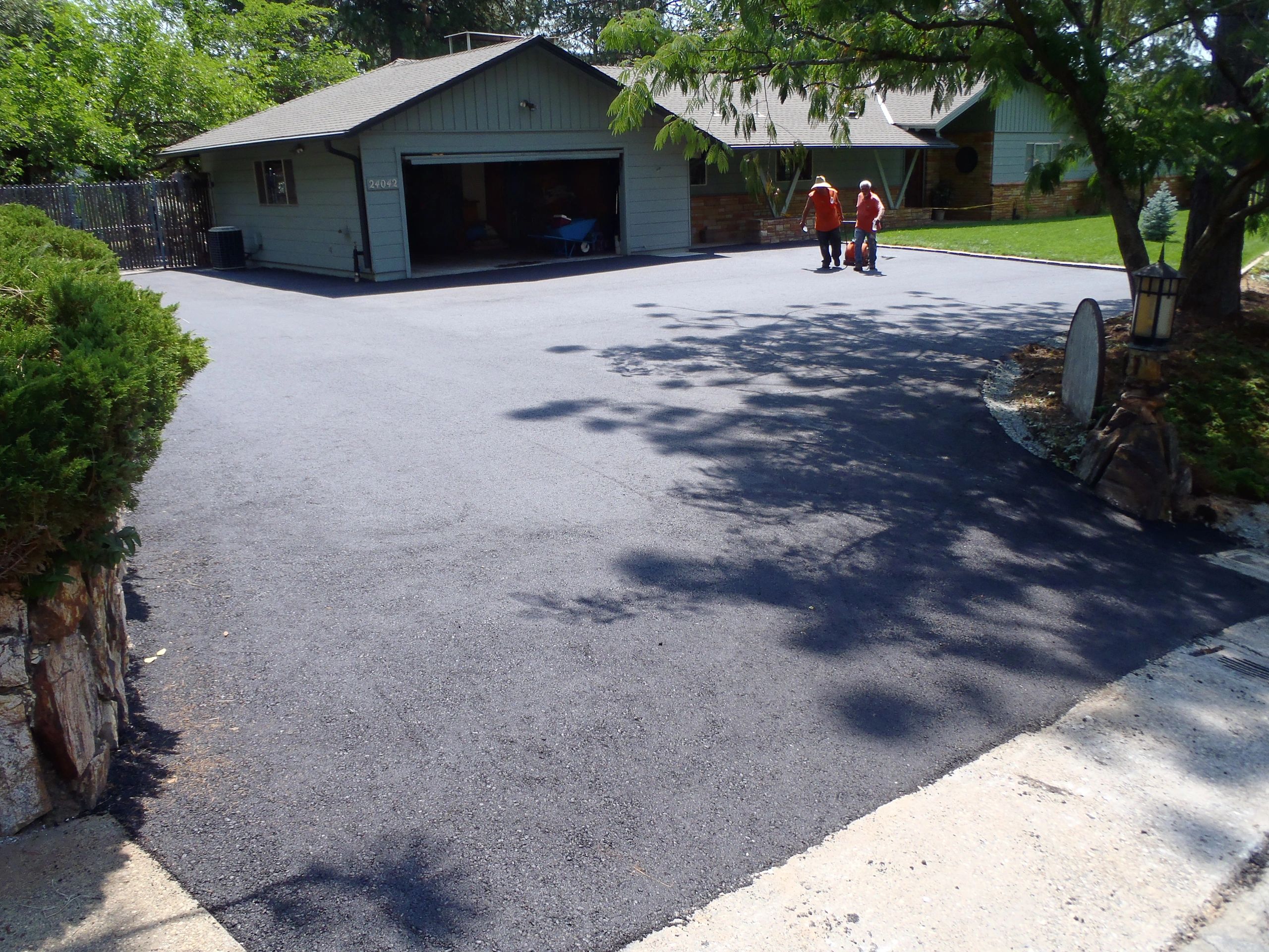 Newly paved asphalt driveway with two crew members and house in the distance