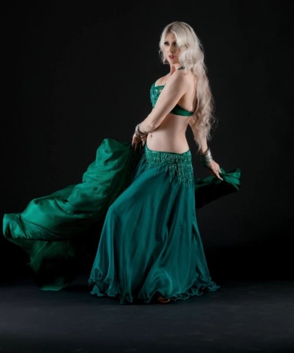 Woman in a green belly dance costume posing against a black background.