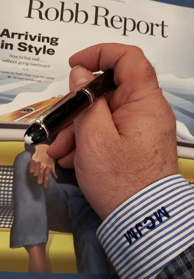 The shirtsleeve of Martin Mongiello holding a Montblanc pen over a Robb Report magazine.