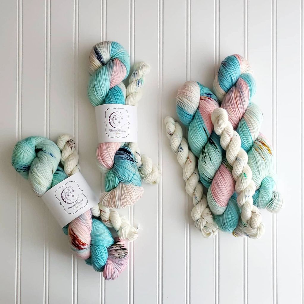Skeins of baby pink, blue and white, with speckles or reds, blues and yellows sit on a white bg.