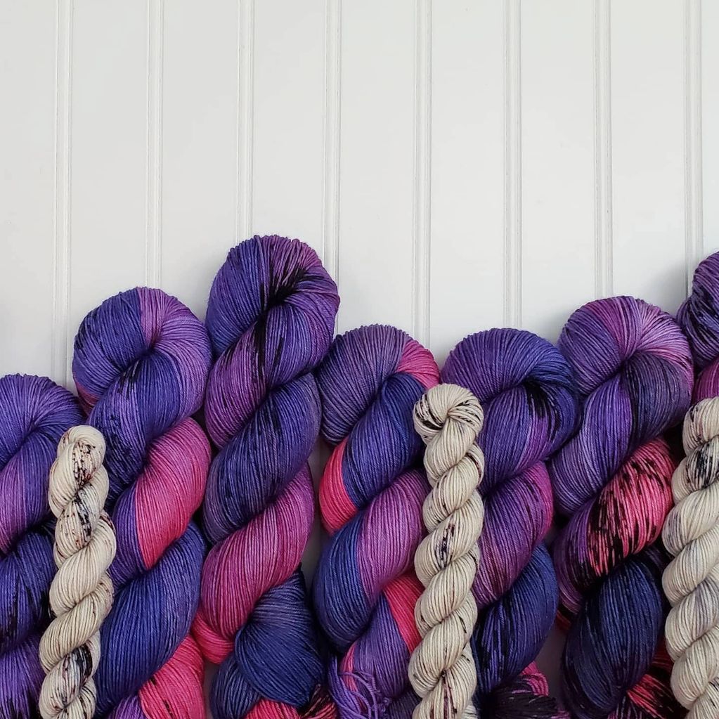Skeins of deep navy, purple and bright magenta line the bottom of the photo, with tan minis on top.