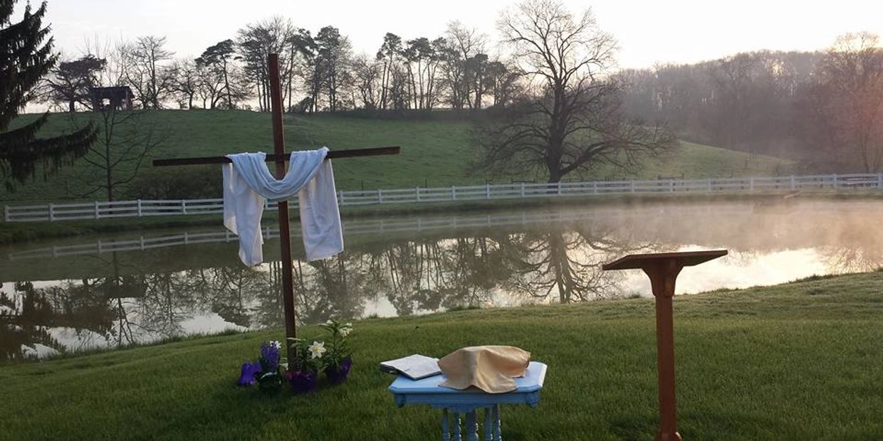 A photo of an outdoor altar with pulpit, communion table, hymnal, and large cross draped in white.