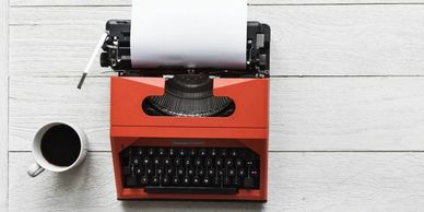 Orange typewriter next to coffee mug on white wood table.