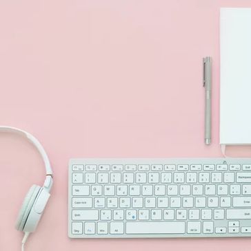 white keyboard, headset, pen, and notepad rest on pink background