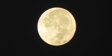 Creamy full moon close up with dark spots and craters visible