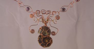 Two ammonite fossils wrapped in copper wire to look like a sea creature. Pendant on wire necklace.