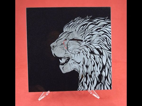 Pen and ink drawing of a lion head laser engraved onto a black granite tile as a piece of art.