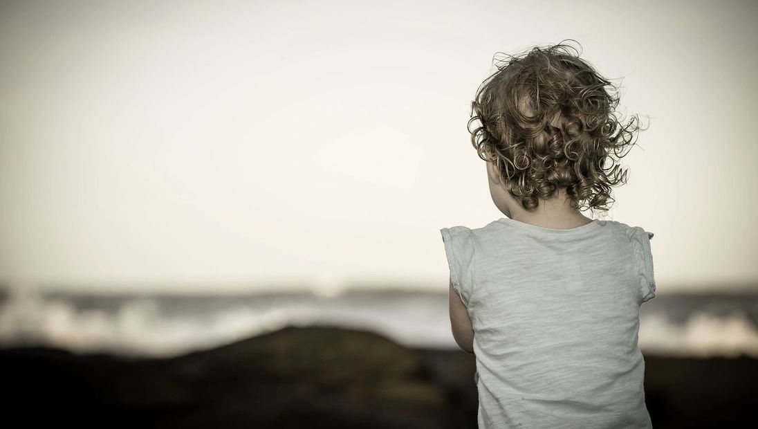 Child with curly hair looking at the ocean.