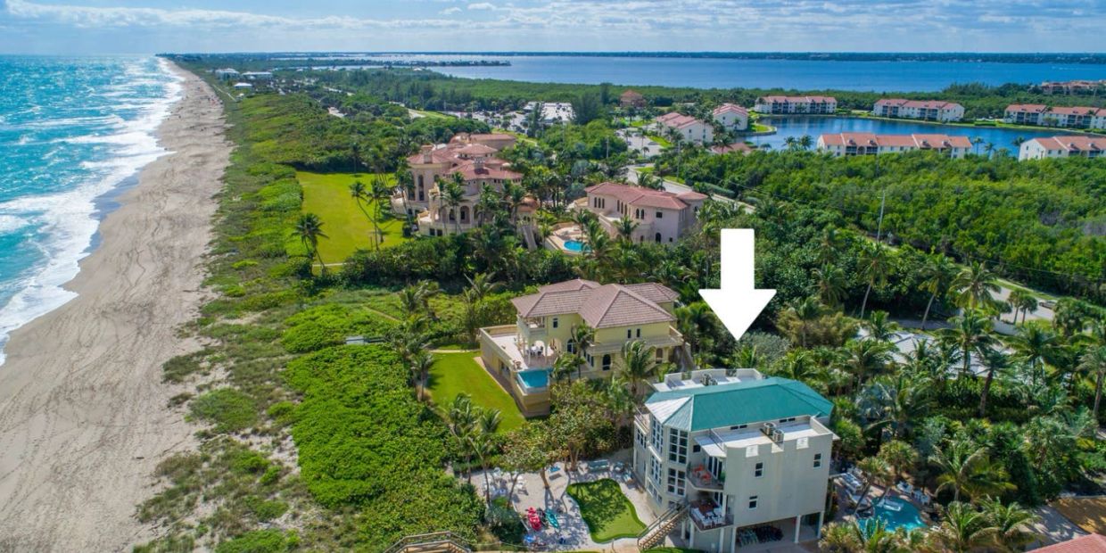 Aerial view of beachfront luxury homes with a white arrow pointing to one house.