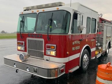 Red fire truck parked on wet pavement with orange cones nearby.
