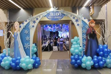 Frozen-themed birthday party entrance with Elsa and Anna cutouts and blue balloons.