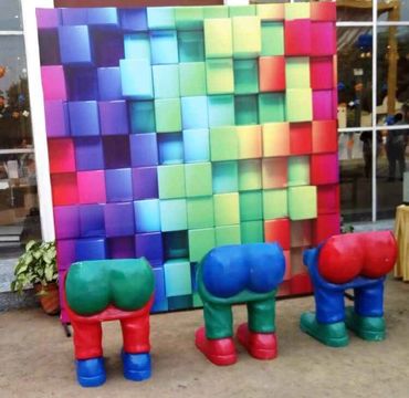 Colorful sculptures resembling bent-over legs in front of a vibrant pixelated wall.