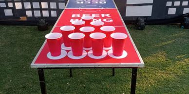Outdoor beer pong setup with red cups on a table on grass.