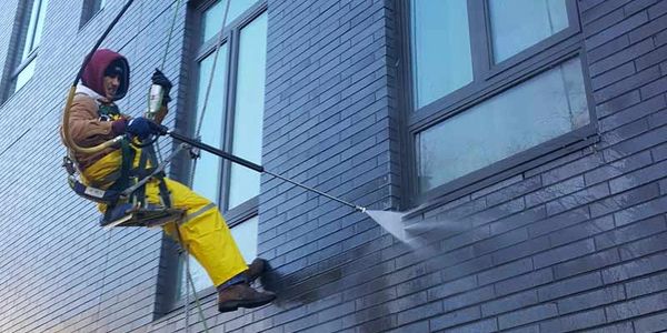 Suspended worker pressure washing a brick building