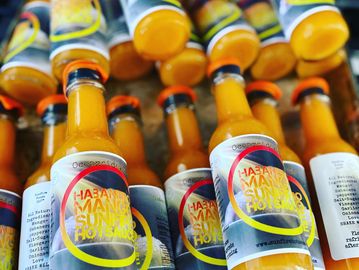 Bottles of bright orange hot sauce with vibrant labels stacked together.