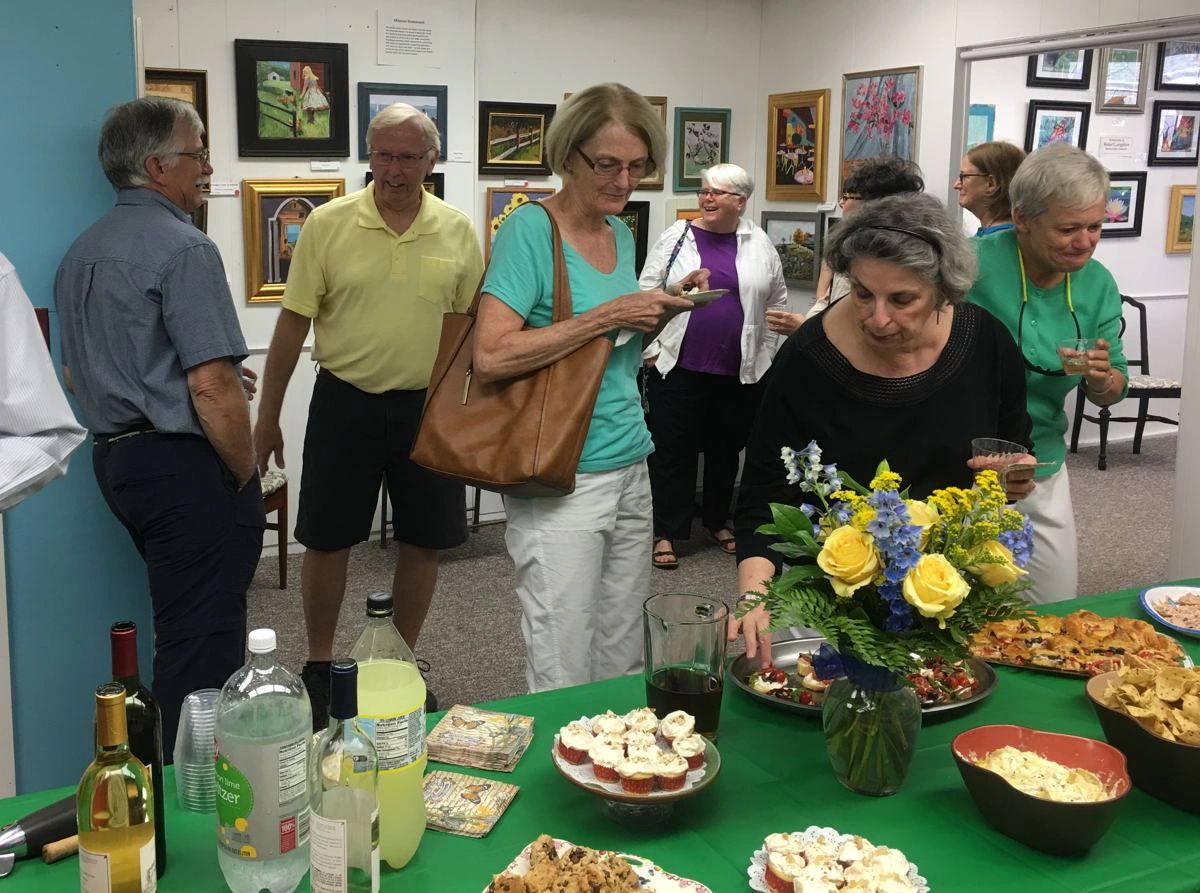 three women at the buffet table at an art reception with other guests in the background
