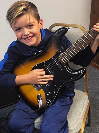 Young student learning to play guitar with a big smile on his face at the Norman Music Institute