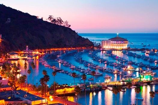 A vibrant marina at dusk with boats and illuminated waterfront buildings.