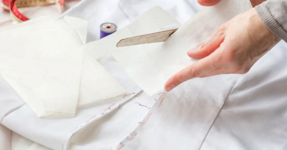 Hands cutting white fabric with scissors.