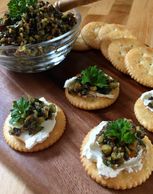 Olive tapenade served on a cracker with cream cheese and garnished with parsley.