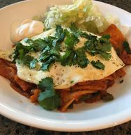 Chilaquiles for Breakfast served with a fried egg, cilantro, iceberg lettuce, and sour cream.
