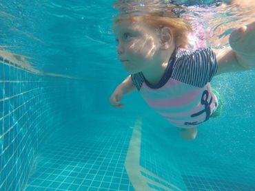 Little girl with blonde hair swimming underwater in pink, blue and white Anker swimsuit.