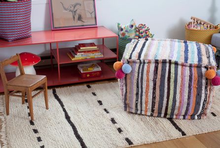 Moroccan rug and pouf with pom-poms, hand-loomed in Morocco with ornate patterns & colorful stripes.