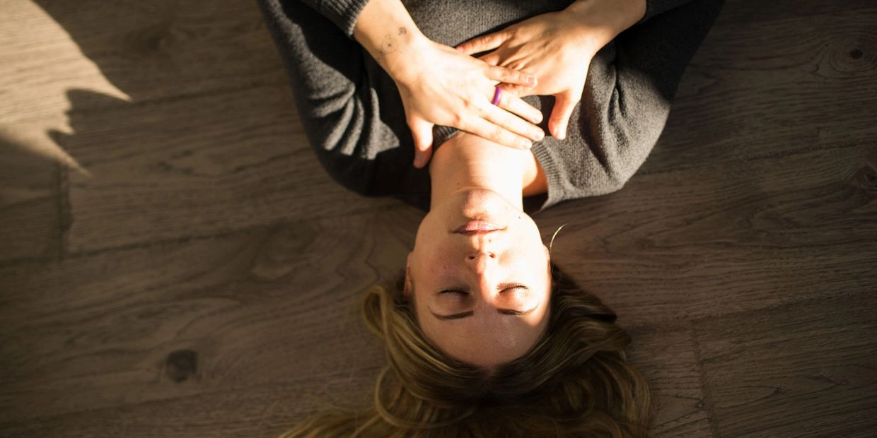 A woman lying on floor with hands holding throat chakra
