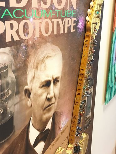 Close up of digital poster and artwork title written with found scrabble letters on guitar neck.