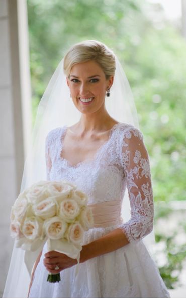 A smiling bride in a lace wedding dress holding a bouquet of white roses.