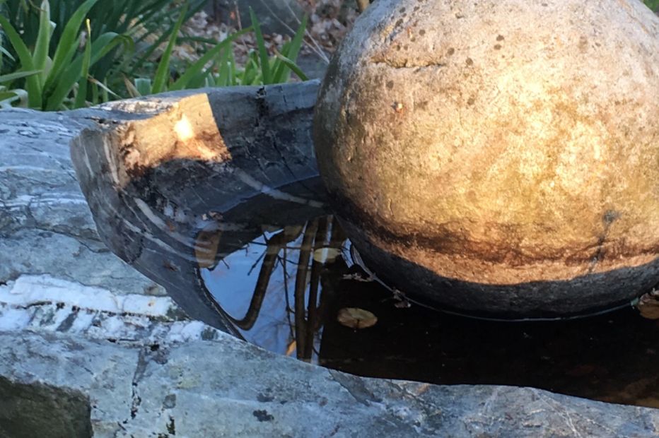 Rock cut basin sculptures inspired by nature adorns the garden in my fundamental landscape design approach. The power of nature is reflected in the swirling waters that can shape even the most jagged stones, resulting in rocks that are smooth to the touch and pleasing to the eye. Pictured here is a stone sphere resting in a rainwater filled crescent shaped stone basin.