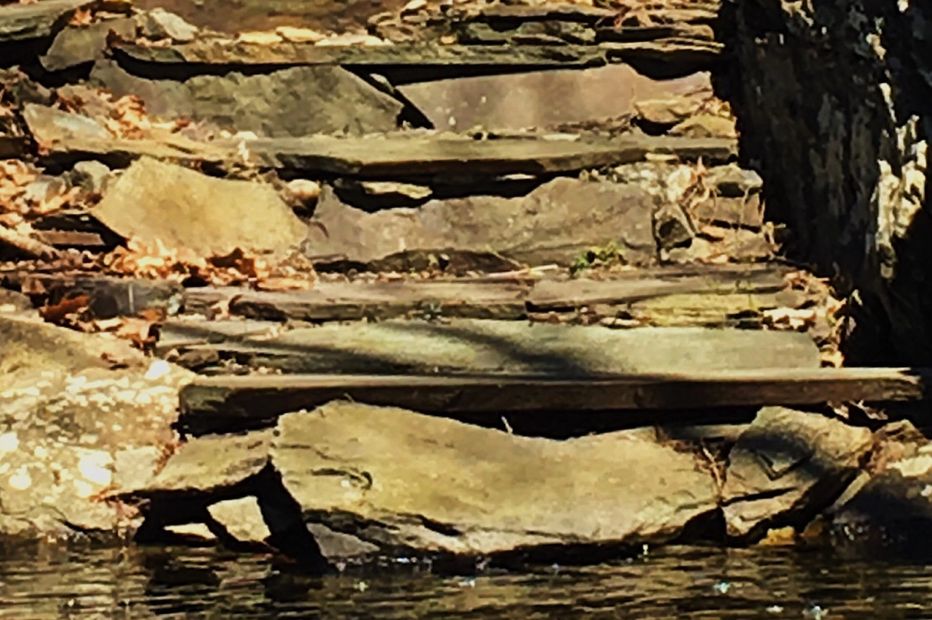 Stones steps leading to a swimming hole at its base is designed to be part of the natural landscape blending with the temptation of water to create an alluring hideaway in this landscape design.