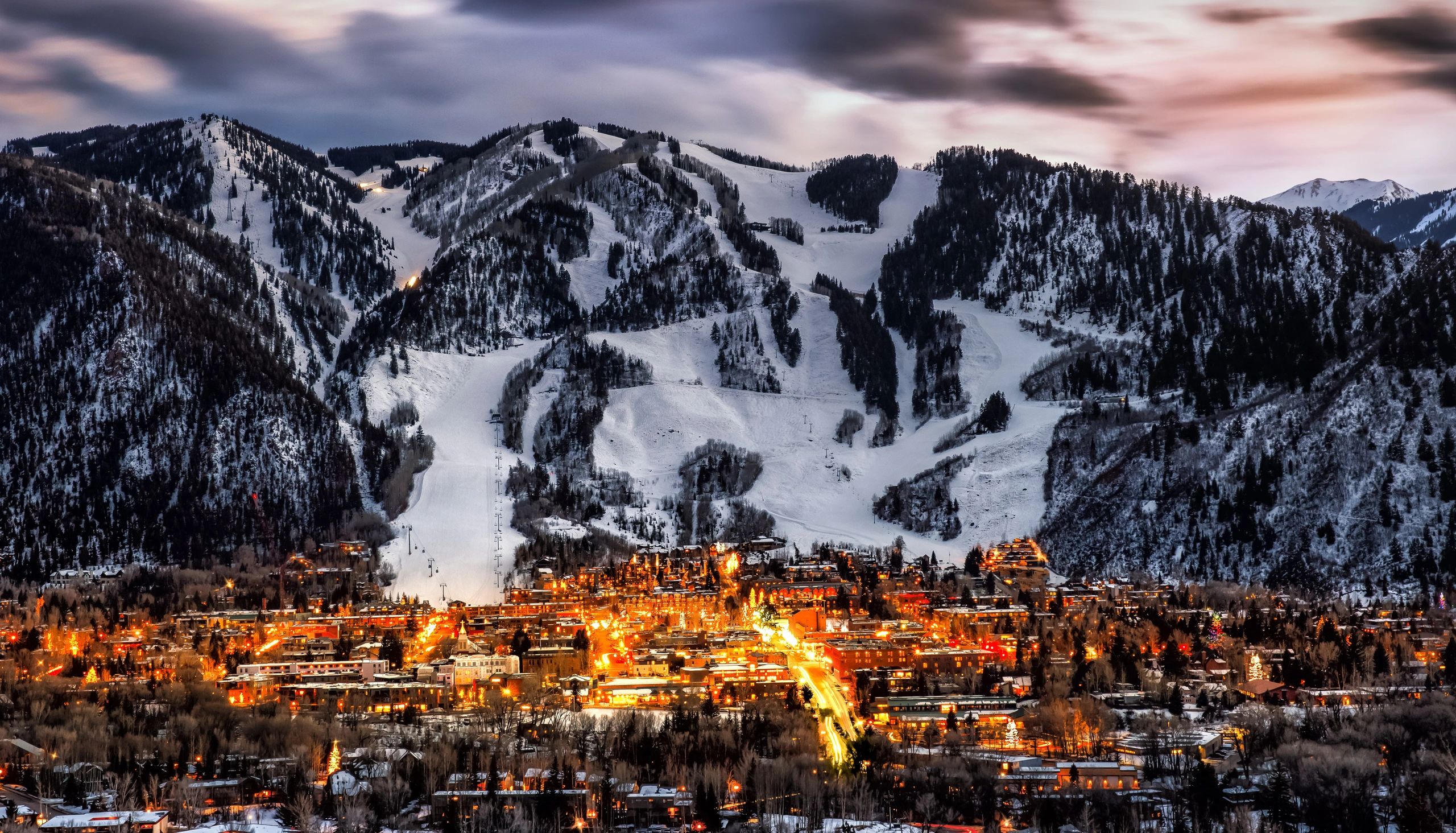 Snow-covered ski resort town at dusk with mountains in the background.