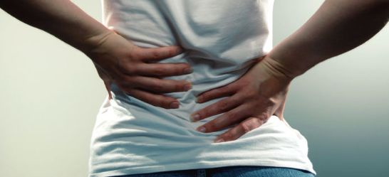 A woman in a white t-shirt holds her lower back in pain