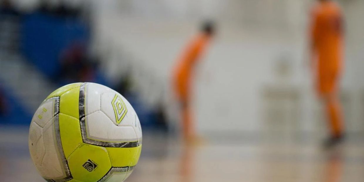 Futsal ball in the foreground of a court with blurred futsal players in the background.