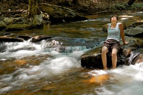 Middle-aged woman sitting on a rock looking heaven-ward in the middle of a gently tumbling waterfall