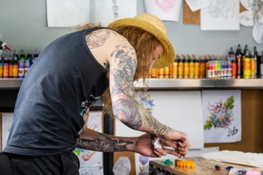 A person with body tattoos checking tattoo inks on the table