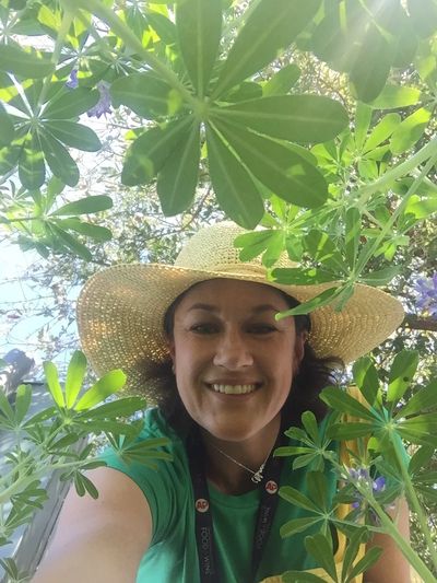 Joelle Kohn homeschool gardening smiling with a hat in a garden of plants