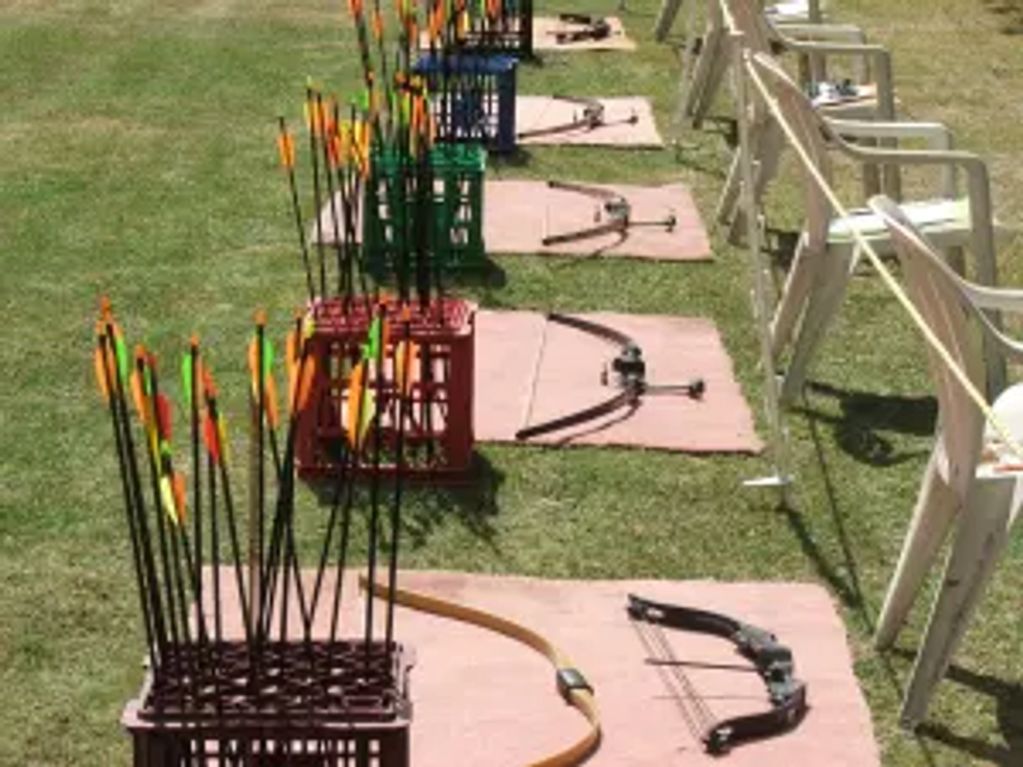 Archery bows and arrows neatly arranged on mats outdoors.