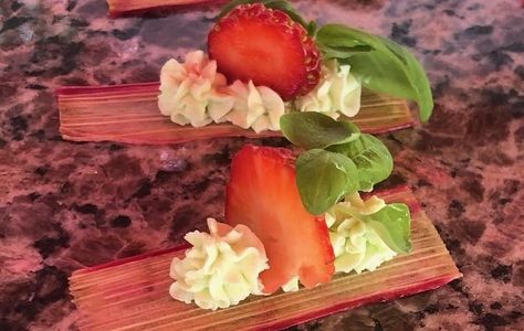 Decorative dessert with strawberries, cream, and green leaves on rhubarb stalks.