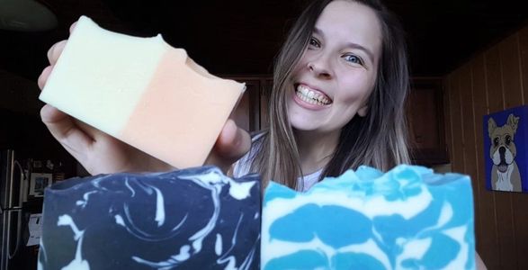 Young woman smiling while holding an orange and white handmade soap.
