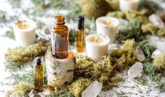 Essential oil bottles surrounded by beautiful light candles, moss and clear quartz crystals