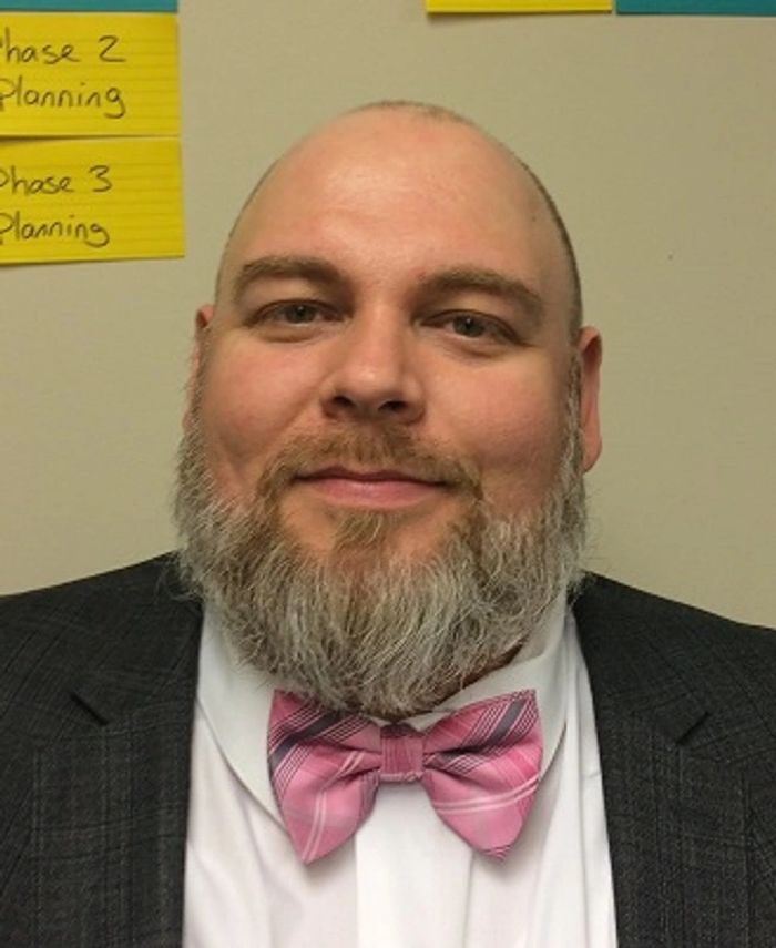 Man with a beard wearing a pink bow tie and suit jacket.